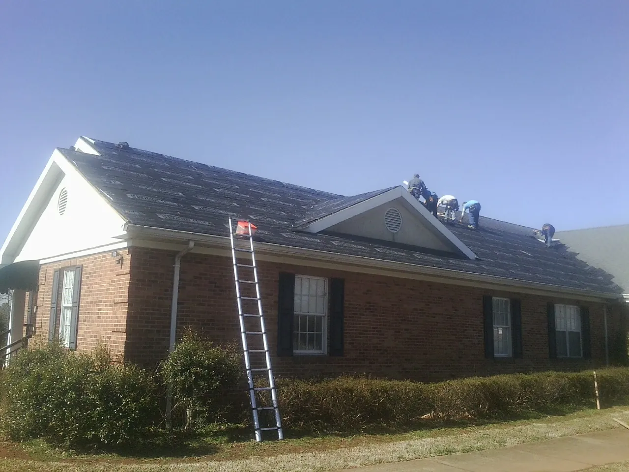 Crew tearing shingles off a brick ranch roof with a ladder set — Metal Roof Repair work by our crew in San Juan Bautista