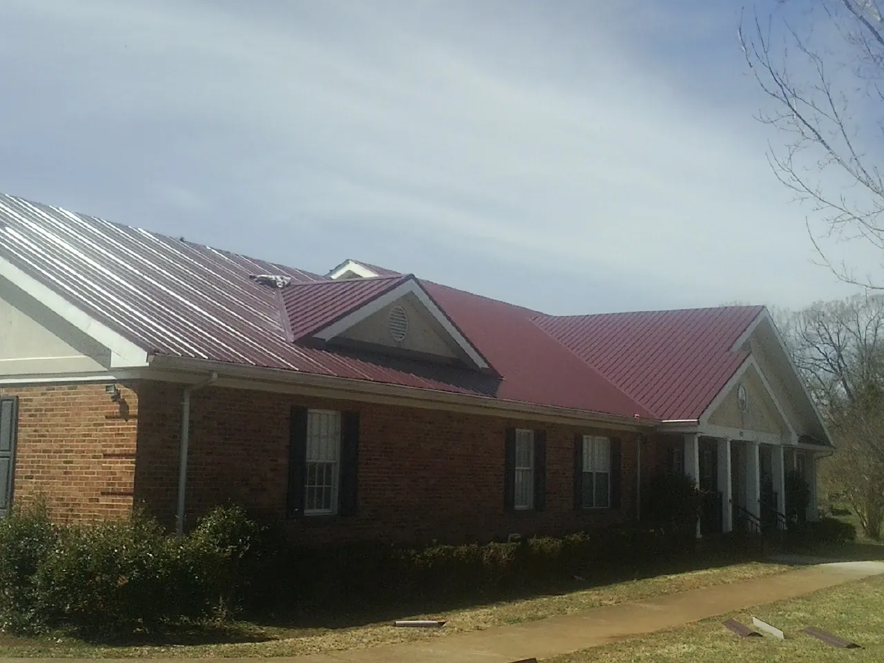 Red metal roof with gabled entries on a long brick building, from a Hail Damage Roof Repair job in San Juan Bautista