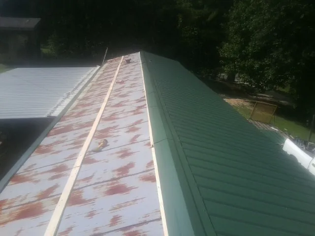 Old rusted panels beside newly installed green metal roofing — Wind Damage Roof Repair by Roofing Brothers in San Juan Bautista