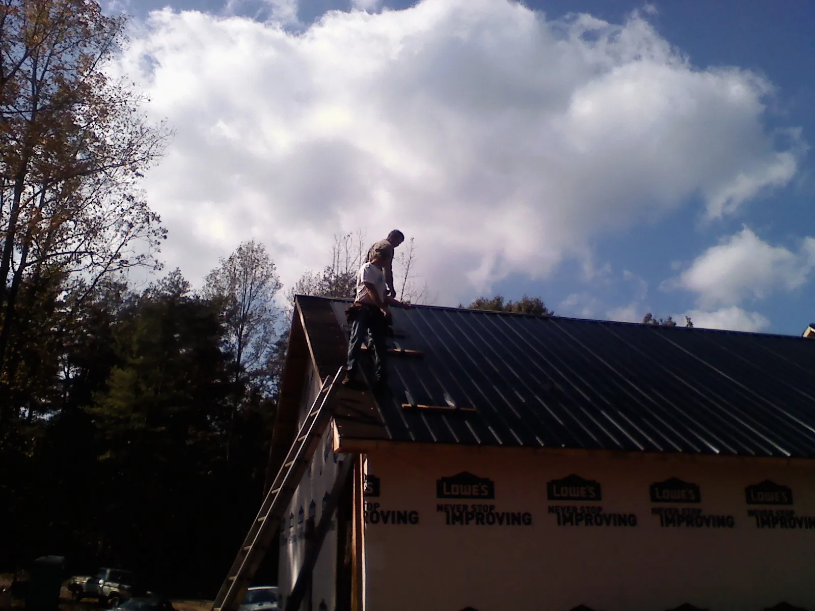 Roofer fastening dark metal panels high against a cloudy sky, from a Roof Inspection job in San Juan Bautista