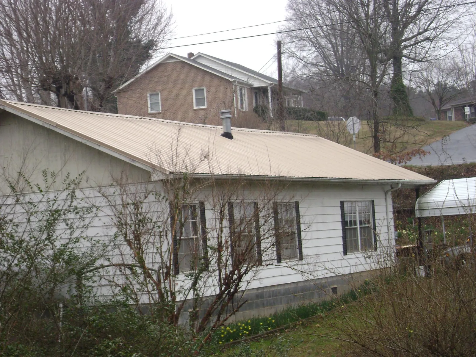 Tan metal roof on a white sided house set into a hillside — Commercial Roofing by Roofing Brothers in San Juan Bautista